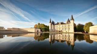 Château Pichon Baron in the sun, perfectly reflected in the body of water before it, located in Medoc, Bordeaux, France.