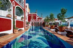 The vibrant, red and white painted walls of Le Sirenuse, surrounding the beautifully tiled pool, decorated with lush plants growing from the clay pots throughout the terrace over the Amalfi Coast, Italy.